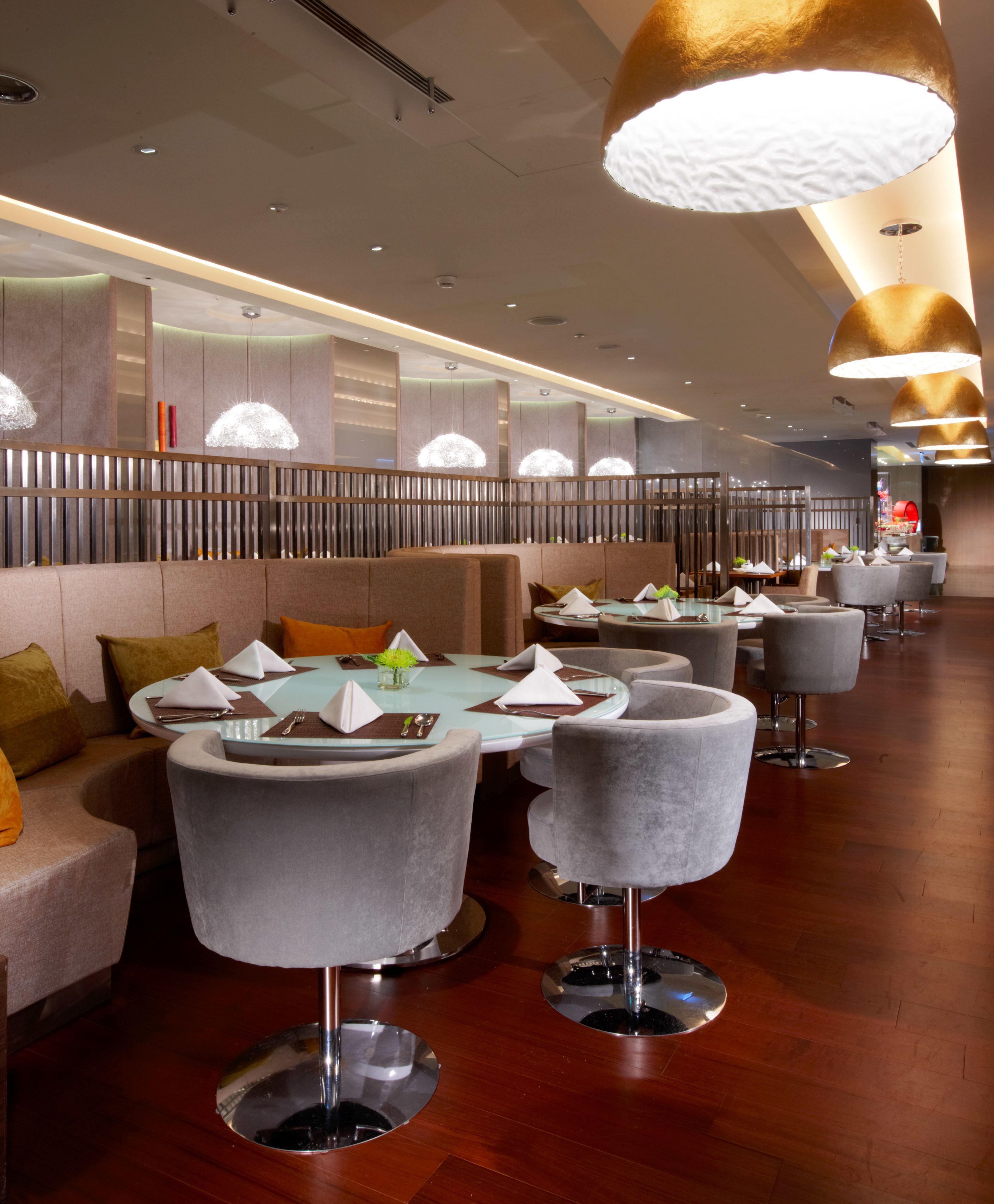 A modern restaurant with round tables and grey upholstered chairs, featuring a wooden floor and ambient lighting.