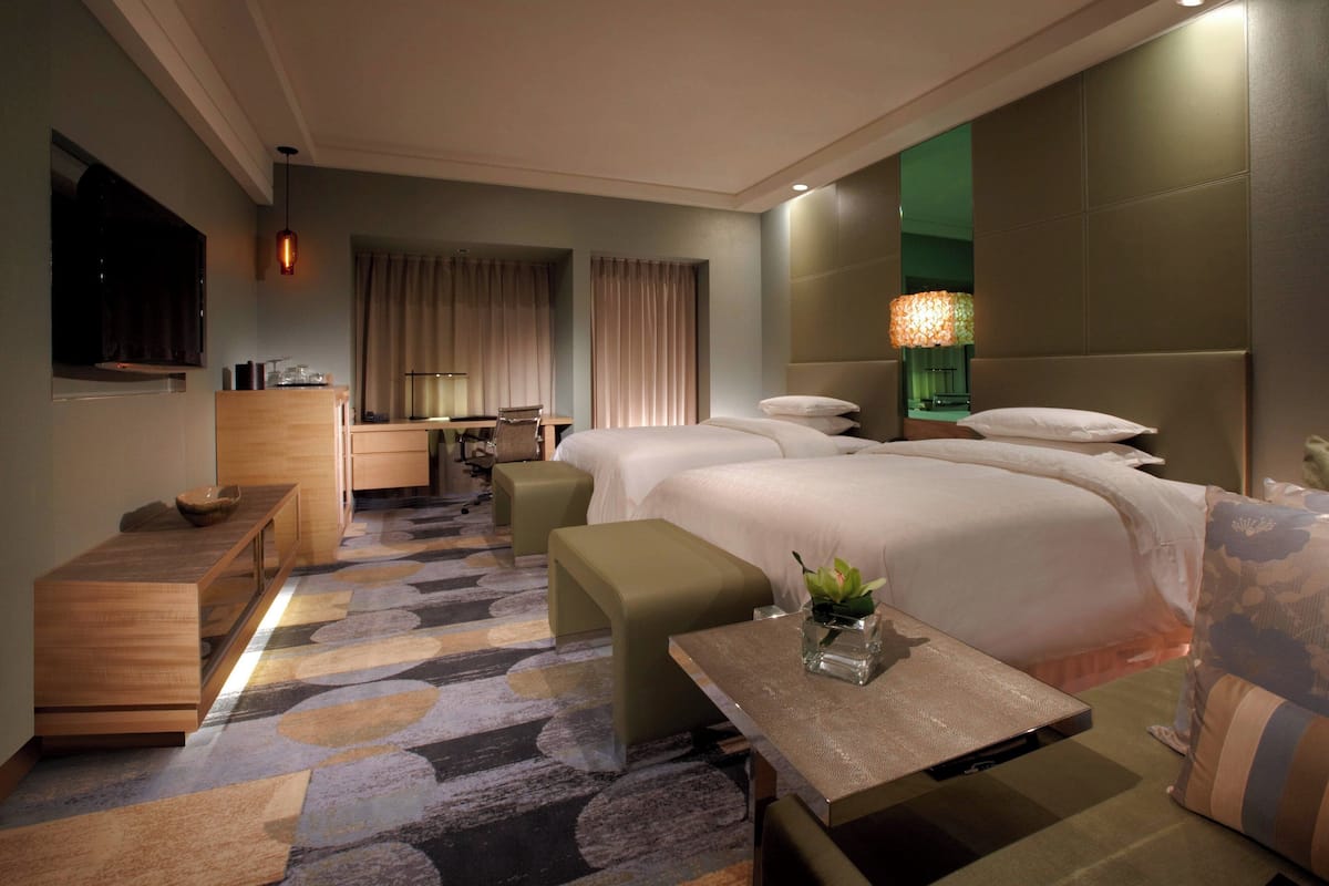 Een hotelkamer met een groot bed, een bureau, een stoel, een tafeltje met een plant en een televisie.