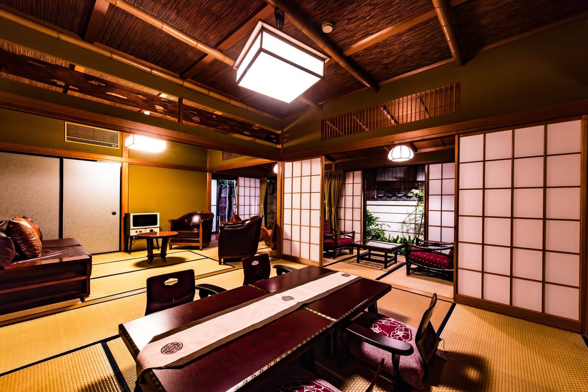 Una habitación japonesa tradicional con suelo de tatami, una mesa baja con cojines, un televisor y puertas correderas que dan a un balcón.