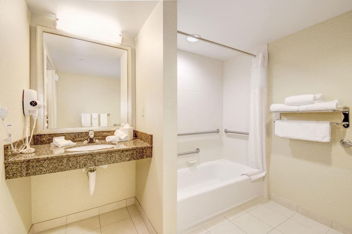 A bathroom with a sink, mirror, towel rack, and shower.