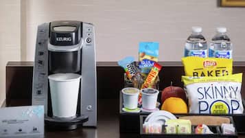A coffee maker, a cup, snacks, and bottled water on a counter.