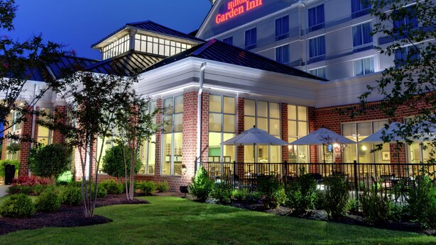 A Hilton Garden Inn with a brick facade, large windows, and outdoor umbrellas. - Hilton Garden Inn Waldorf (Waldorf)