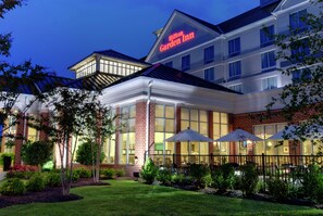 A Hilton Garden Inn with a brick facade, large windows, and outdoor umbrellas.
