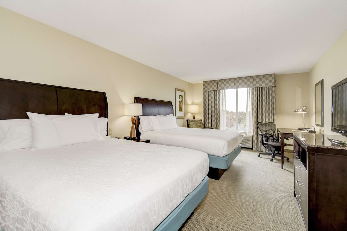 A hotel room with two large beds, a desk, a chair, and a television.