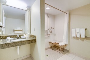 A bathroom with a granite countertop sink, a mirror, a towel rack, and a shower area with a glass door.
