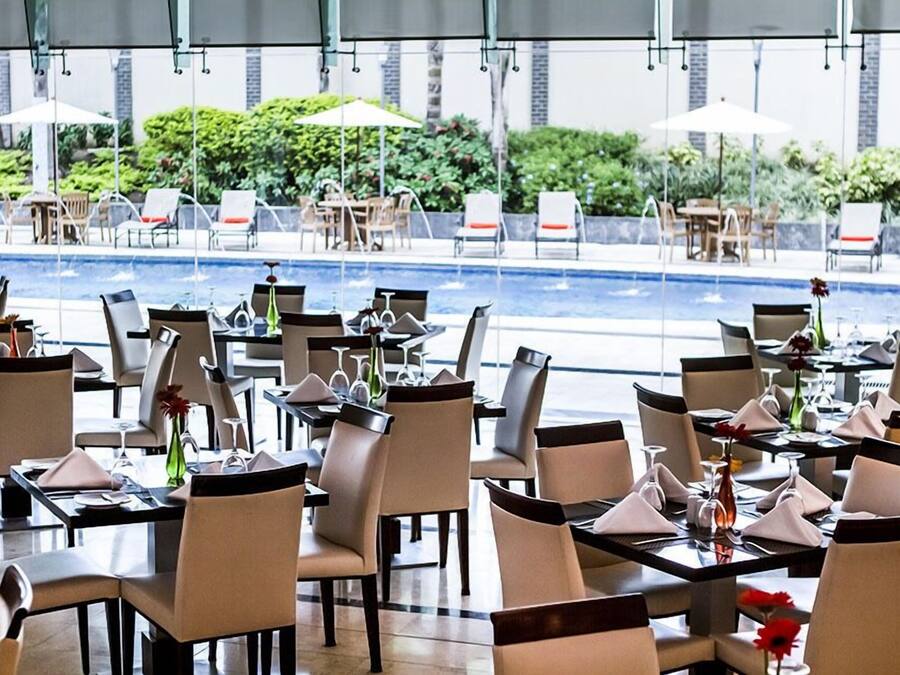 En restaurang med uteservering med utsikt över en pool, med bord, stolar och parasoller.