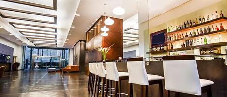 Un área de bar moderna con una barra larga, varios taburetes y una variedad de botellas en estanterías.