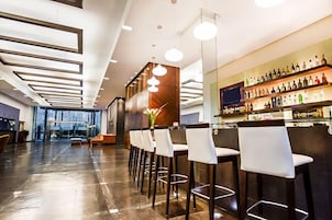 Uma área de bar moderna com um balcão extenso, vários bancos altos e uma variedade de garrafas nas prateleiras.