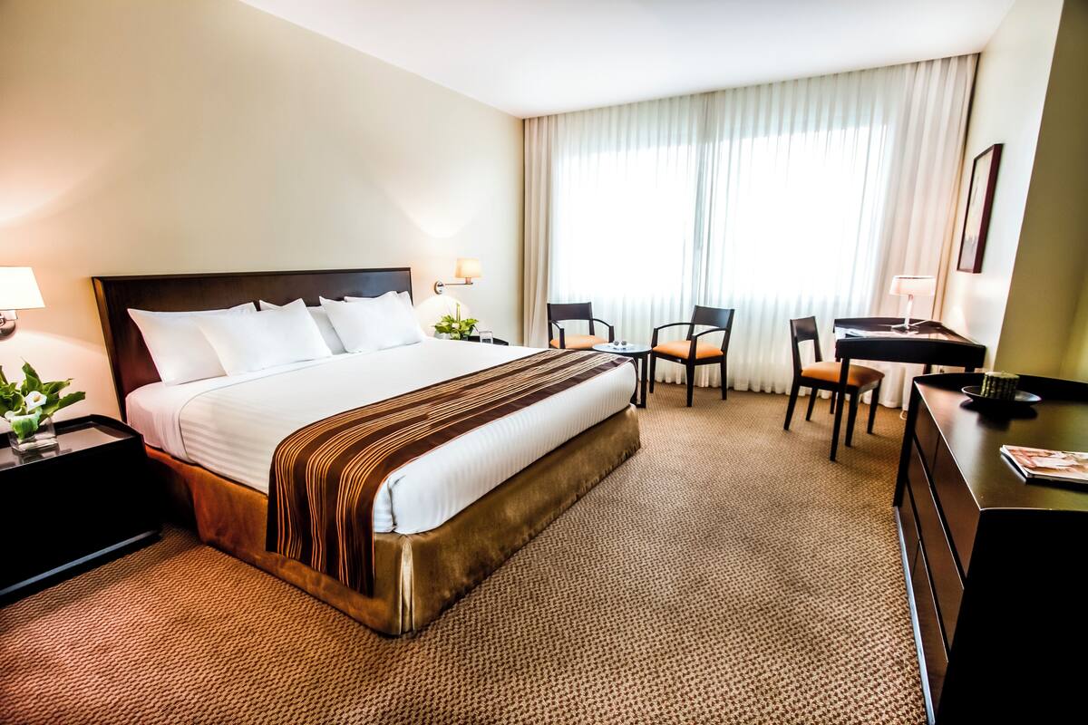 A hotel room with a large bed, a desk, two chairs, and a small table.