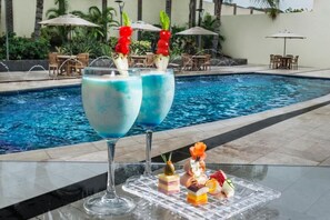 Ein Poolbereich mit zwei großen Gläsern blauer Cocktails, einer Auswahl an Desserts und Gartenmöbeln.