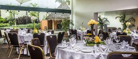 A restaurant with round tables set for dining, featuring white tablecloths and gold chairs.