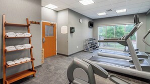Un gimnasio con cintas de correr, un perchero de madera y una ventana con vista a árboles.