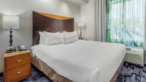Una habitación de hotel con una cama grande, dos mesitas de noche con lámparas, una mesita con teléfono y una ventana con cortinas.