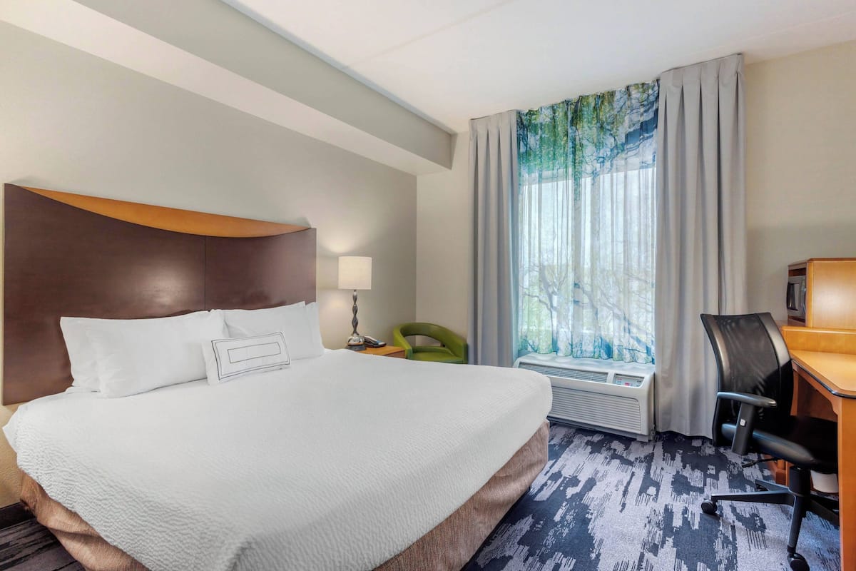 A hotel room with a large bed, a desk, a chair, a lamp, and a window with curtains.