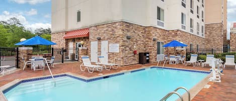 A hotel pool area with lounge chairs and umbrellas, a brick wall, and a sign warning no lifeguard on duty.