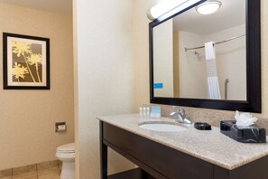 A bathroom with a sink, mirror, and toilet. There is a framed picture on the wall and a towel rack with a towel.