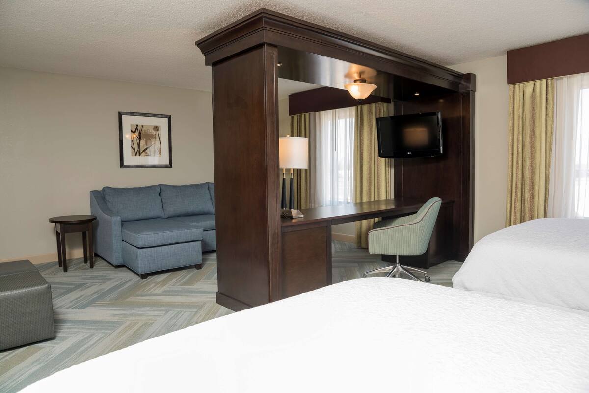 A hotel room with a bed, a desk with a chair, a sofa, a TV, and a framed picture on the wall.