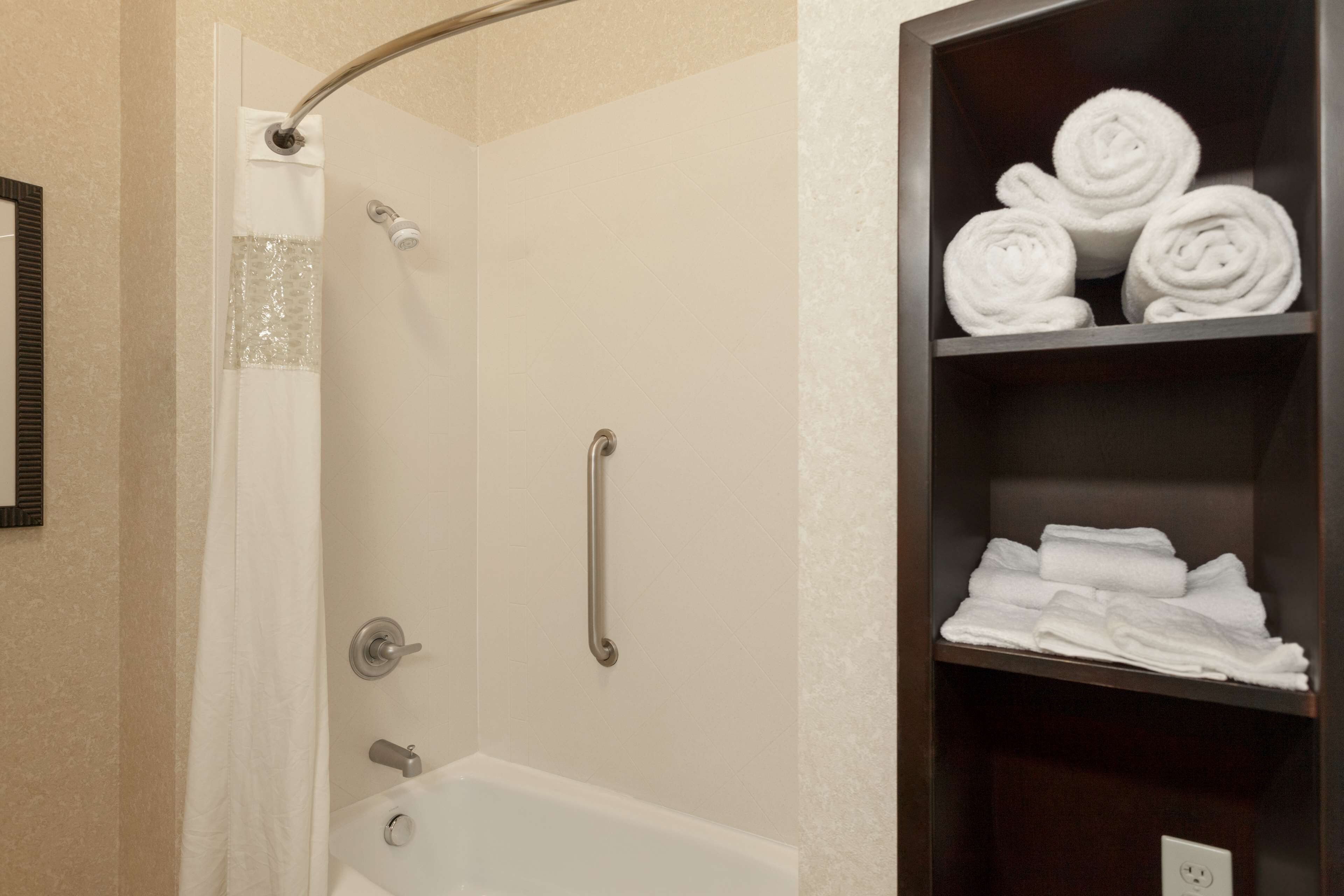 A shower with a handrail, a bathtub, and a shelf with rolled towels.