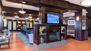 A lobby with a fireplace, seating area, and a television displaying the weather. - Hampton Inn Detroit/Roseville (Clinton Township)
