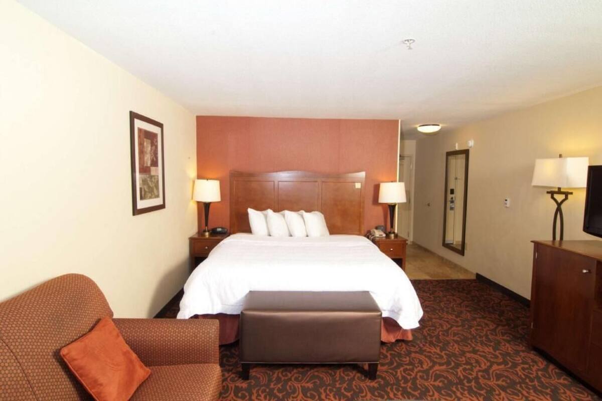 Une chambre d’hôtel avec un grand lit, un canapé, un pouf, une télévision et un miroir.