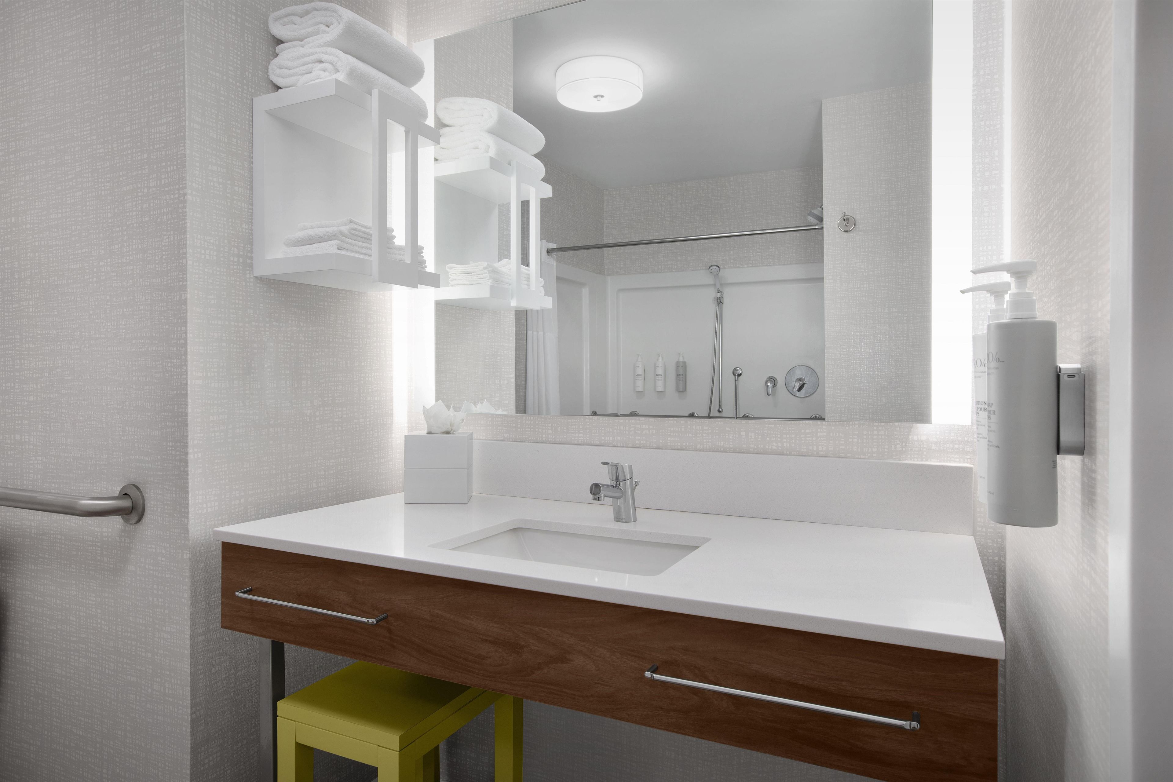 Een moderne badkamer met een witte wastafel, houten opbergmeubel en een spiegel die een douchegedeelte weerspiegelt.