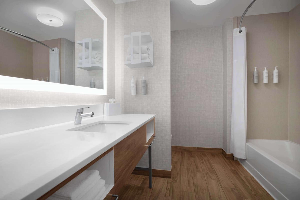 Une salle de bain moderne avec un grand miroir, un lavabo blanc, un meuble-lavabo en bois, une douche et une baignoire.