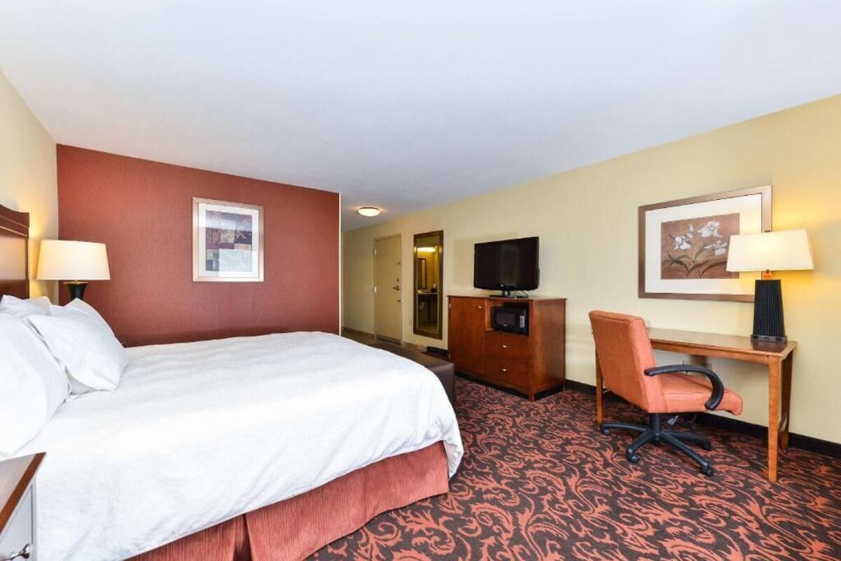 Une chambre d’hôtel équipée d’un lit, d’un bureau, d’une chaise, d’une télévision et décorée avec des œuvres d’art aux murs.