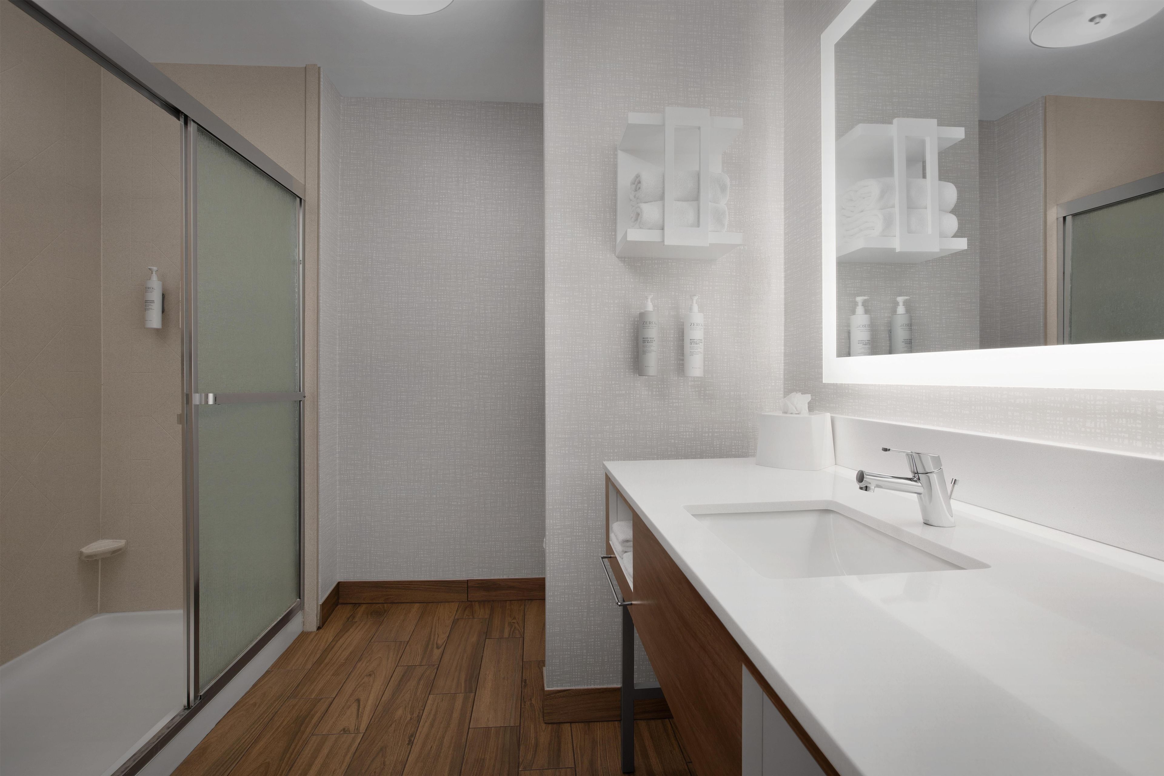 A modern bathroom with a shower, a vanity with a mirror, and toiletries.