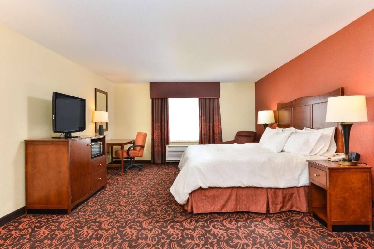 Une chambre d’hôtel équipée d’un lit, d’une télévision, d’un bureau, d’une chaise et d’une fenêtre avec des rideaux.