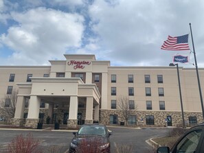 Un hôtel Hampton Inn avec une façade en pierre, une grande entrée et un drapeau américain.