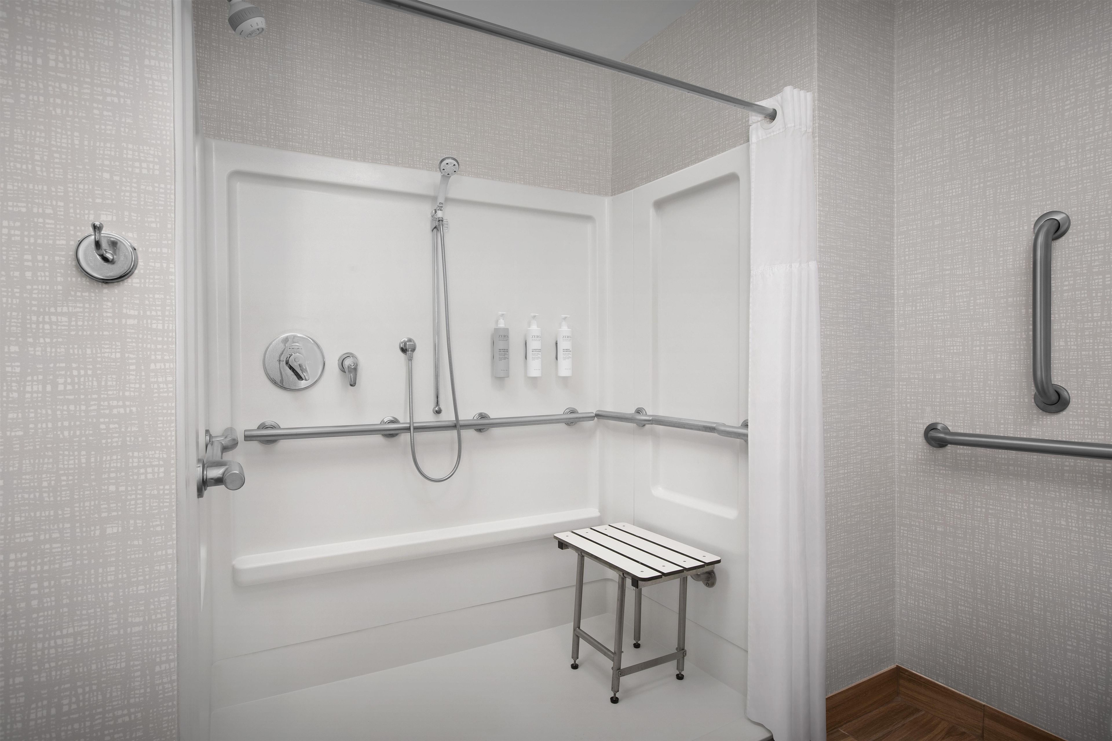 Un baño moderno con ducha a nivel, barras de apoyo, una mesita pequeña y un organizador de ducha.