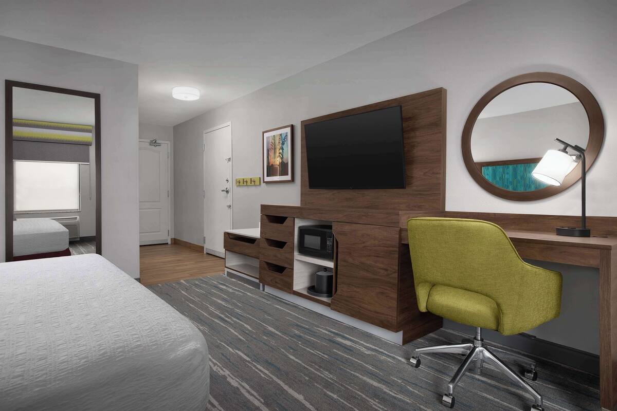 Une chambre d’hôtel équipée d’un lit, d’un bureau avec une chaise, d’une télévision, d’un miroir et d’un four à micro-ondes.