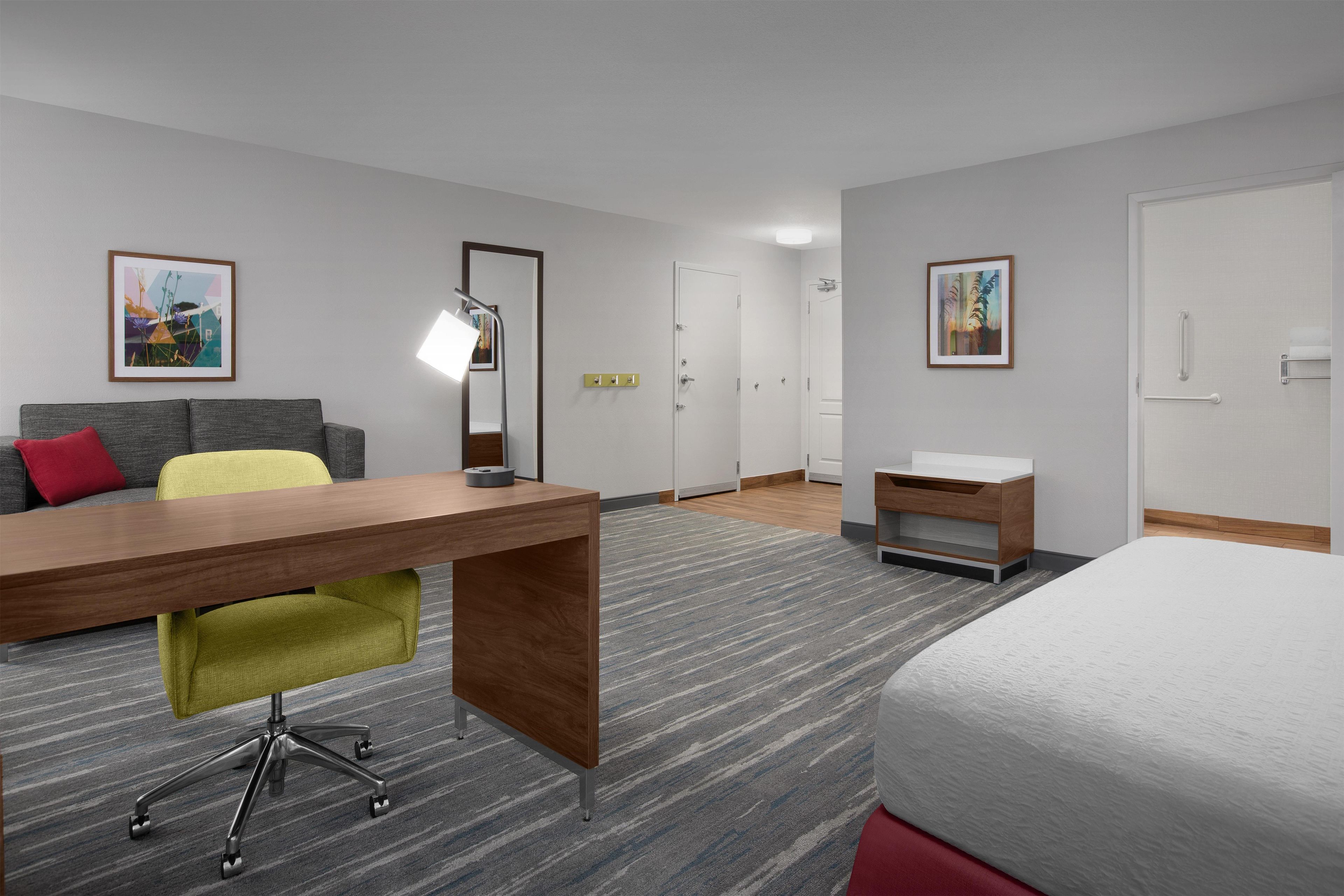 Ein Hotelzimmer mit Schreibtisch, Stuhl, Bett, Nachttisch, Lampe und zwei gerahmten Bildern an den Wänden.