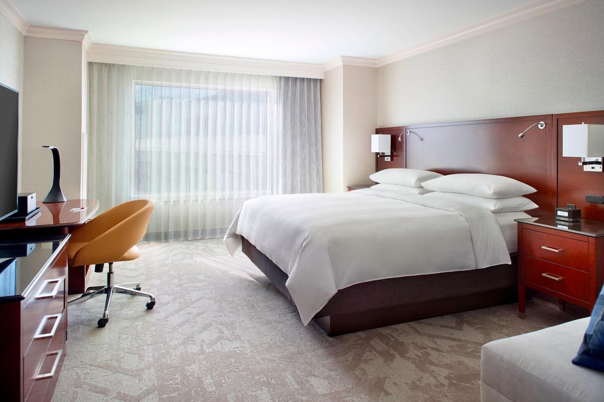 A hotel room with a large bed, a desk with a chair, a TV, and a window with curtains.