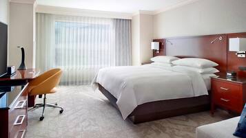 Habitación de hotel con una cama grande, un escritorio con una silla, un televisor y una ventana con cortinas.