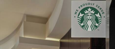 Un letrero de Starbucks en un interior moderno con techo curvo e iluminación colgante.