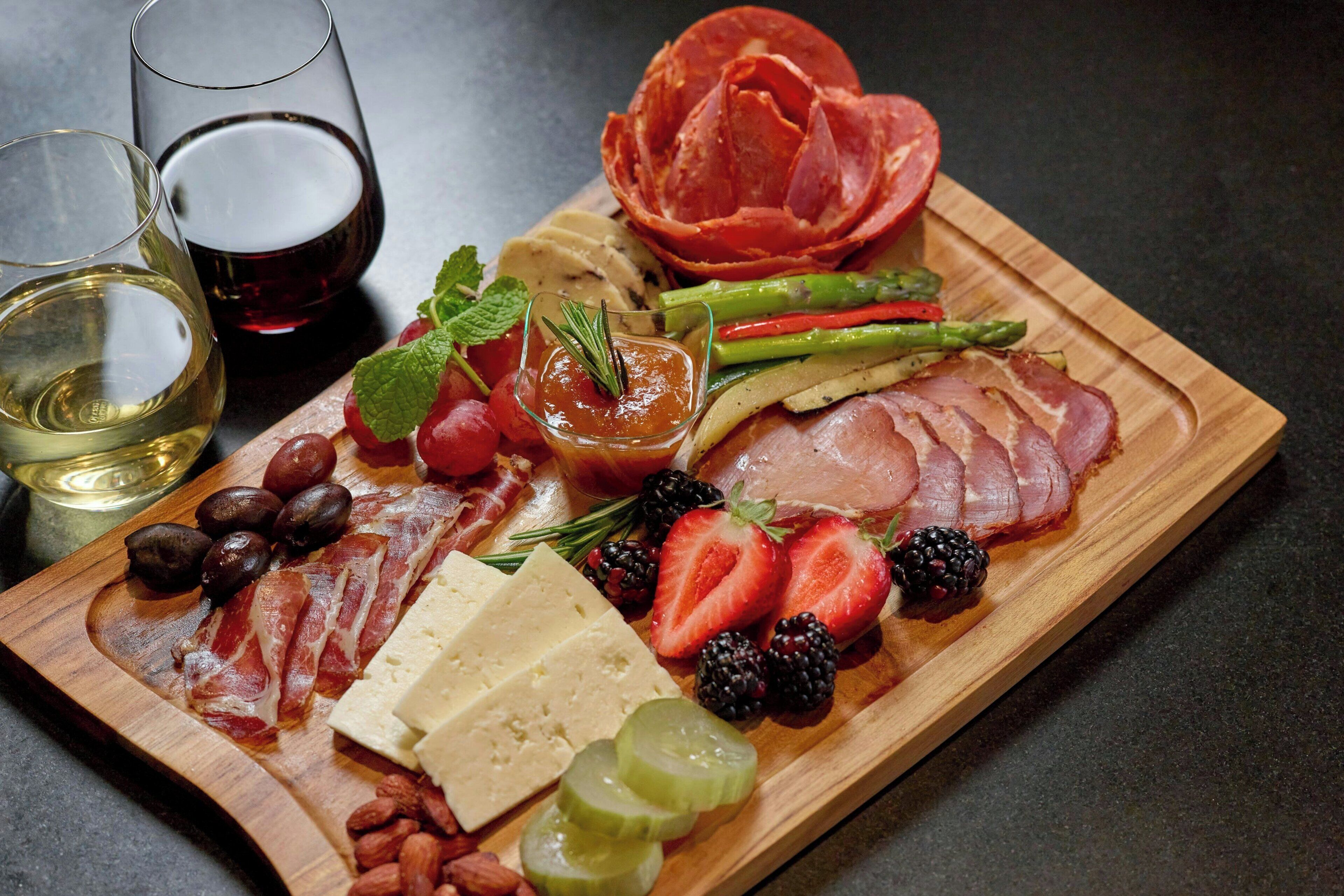 A charcuterie board with various meats, cheeses, fruits, and olives.