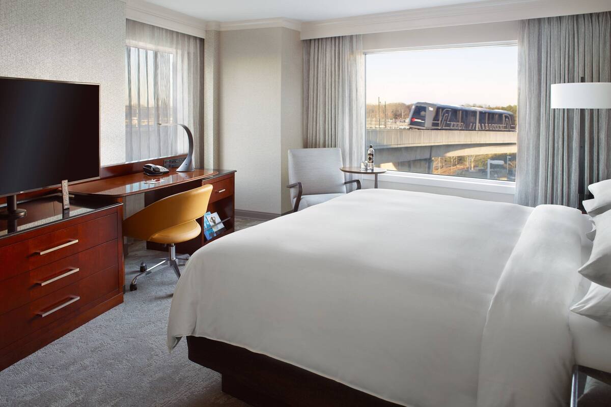 Una habitación de hotel con cama, escritorio, silla, televisor y ventana con vista a un puente.
