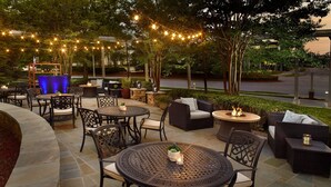 An outdoor patio area with round tables and chairs, string lights, and a fire pit. - Atlanta Airport Marriott Gateway (College Park)