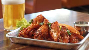 Una bandeja de alitas de pollo con vegetales y una jarra de cerveza sobre una mesa de madera.