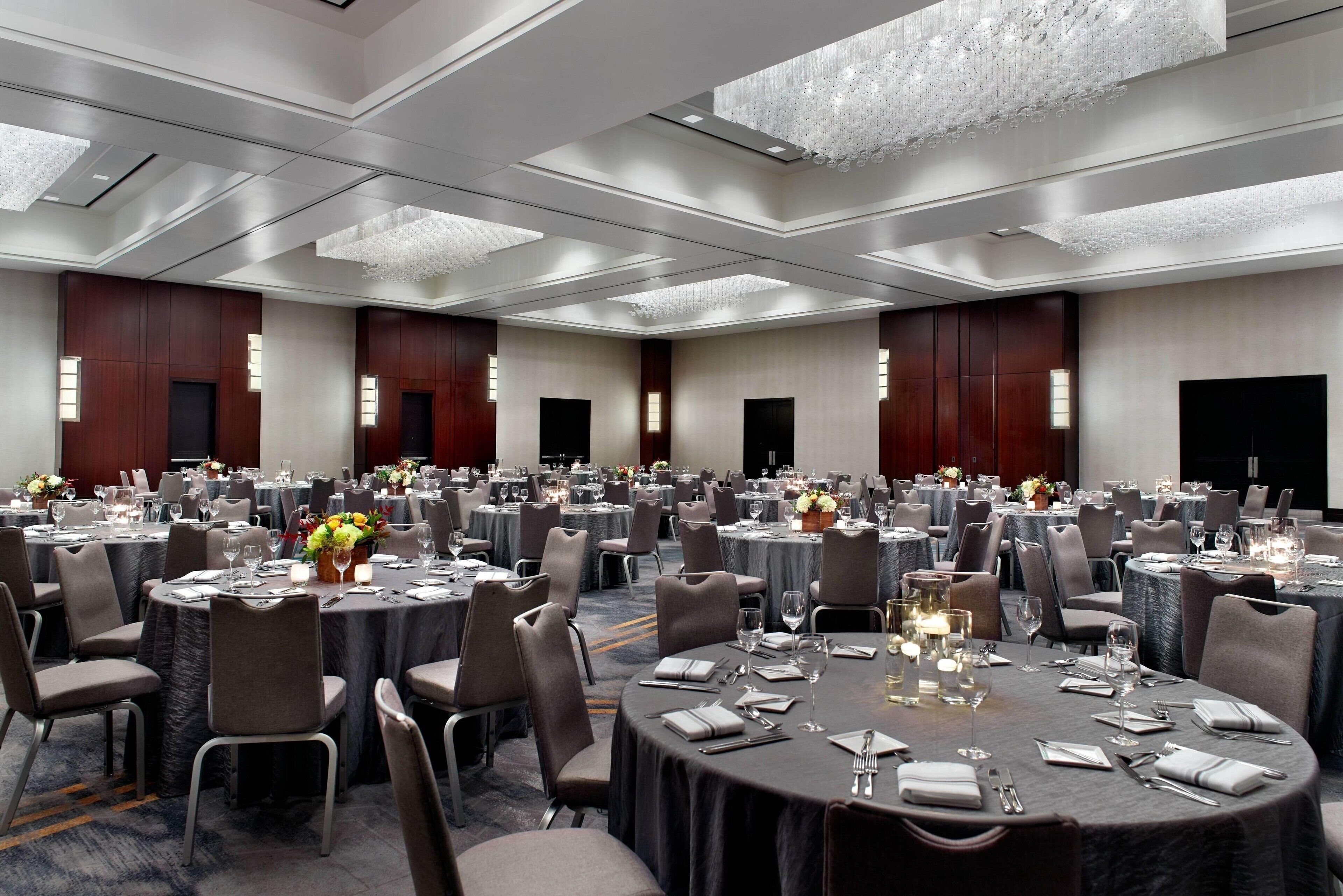 Une grande salle de banquet avec des tables rondes, des chaises et des lustres.