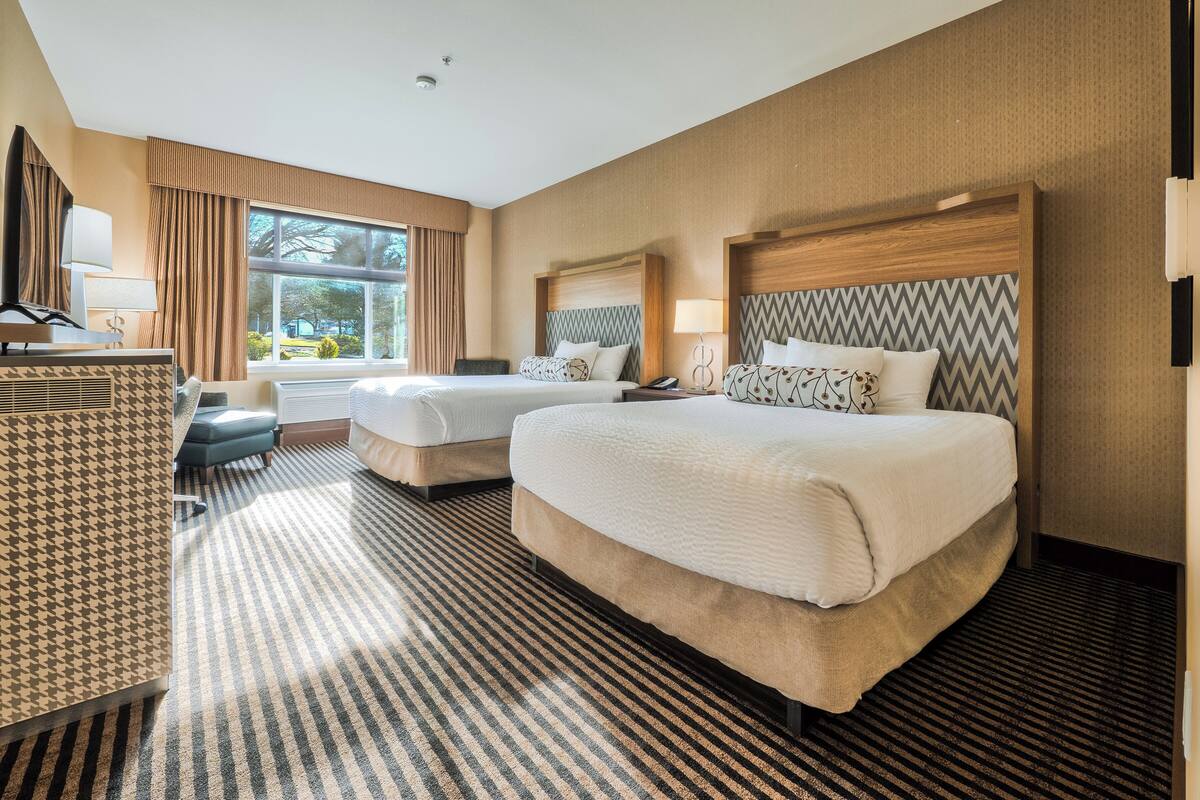 A hotel room with two beds, a desk, a chair, and a large window.