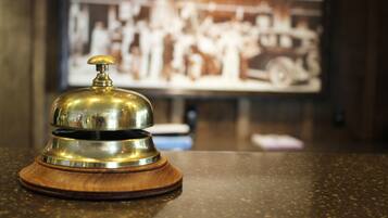 A brass bell on a wooden base, likely a hotel reception bell, with a blurred background featuring a vintage photograph.