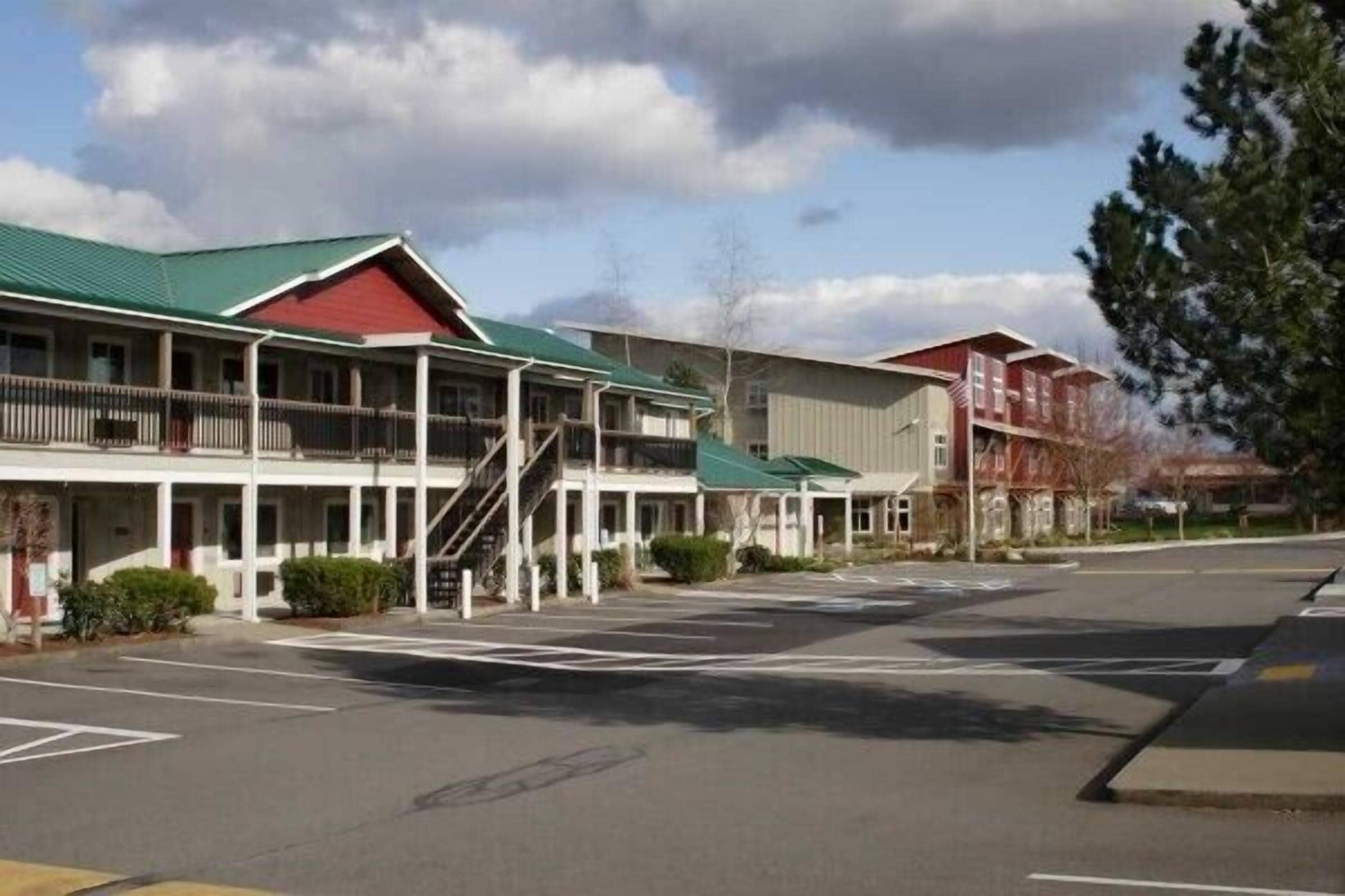 A motel with a green roof, a covered outdoor area, and a parking lot.