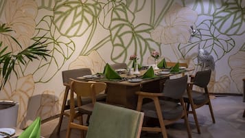 A dining area with a table set for four, surrounded by chairs, and a wall with a leafy pattern.