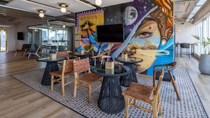 Un interno moderno con tavoli rotondi, sedie in legno, un murale e una TV a parete.