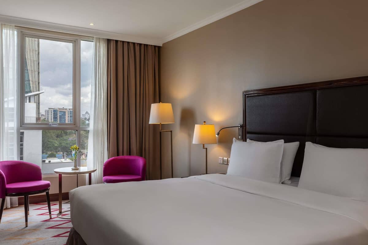 Een hotelkamer met een groot bed, twee stoelen, een tafeltje en een lamp.