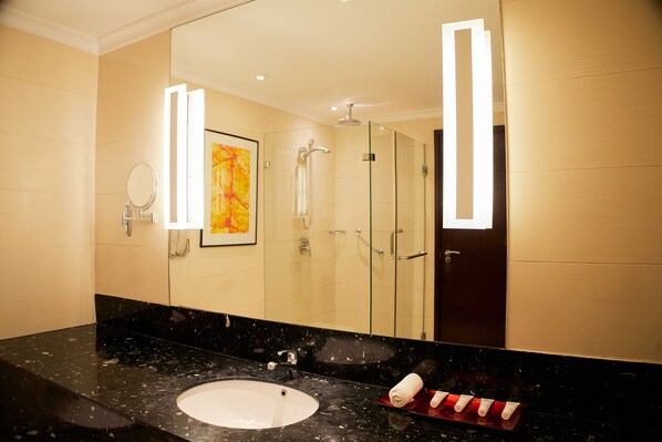 A modern bathroom with a black marble sink, a large mirror, a glass shower enclosure, and a framed artwork on the wall.
