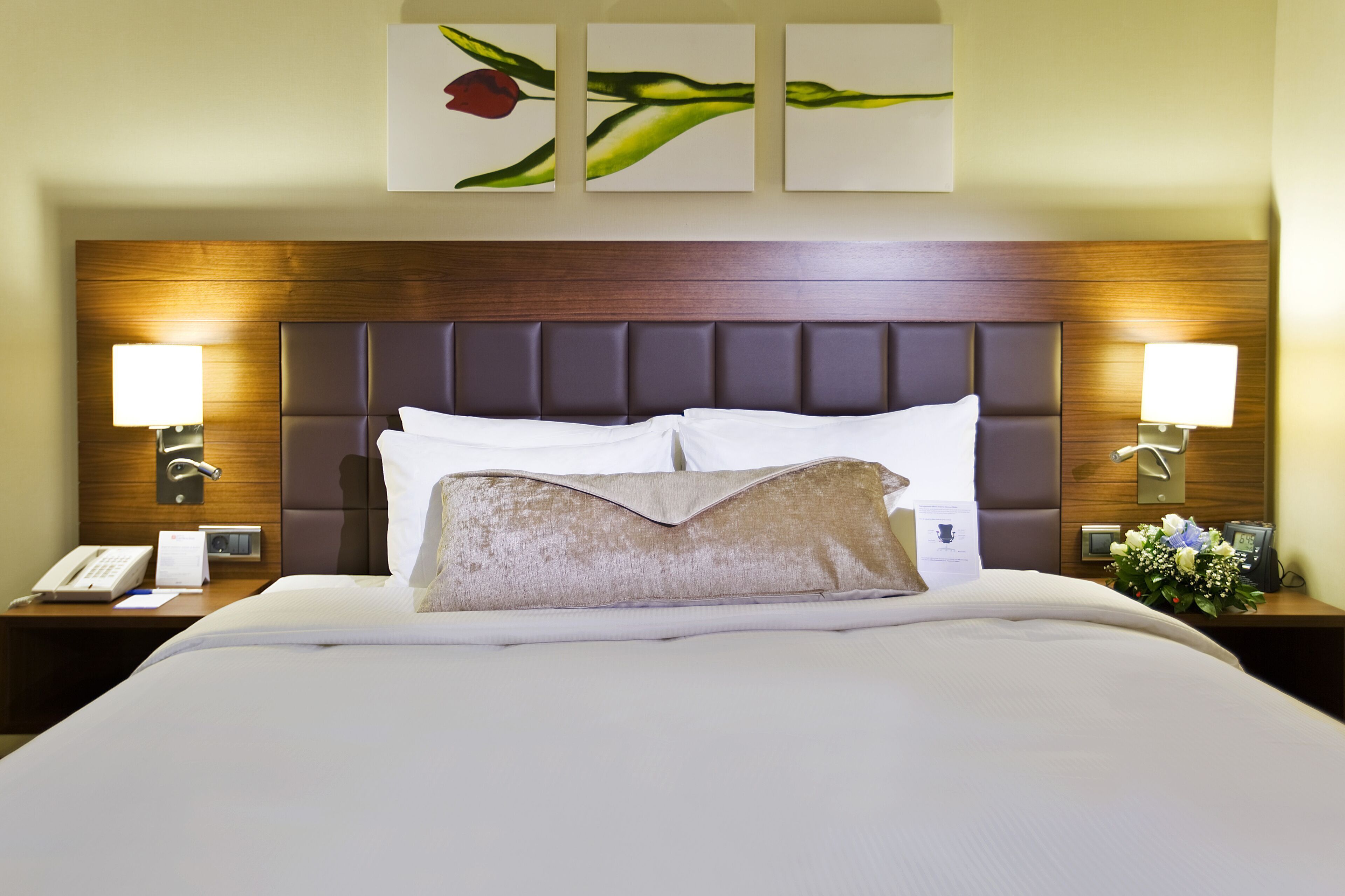 A hotel room with a large bed, two bedside lamps, a wooden headboard, and wall art.