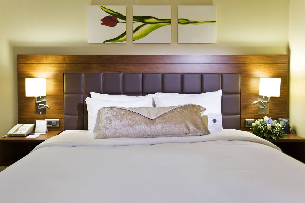 A hotel room with a large bed, two bedside lamps, a wooden headboard, and wall art.